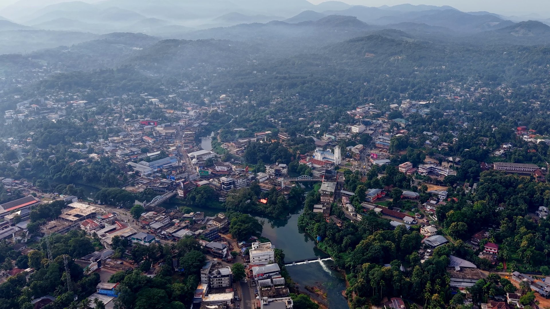 A high view over a town, a river and forested hills in morning haze
