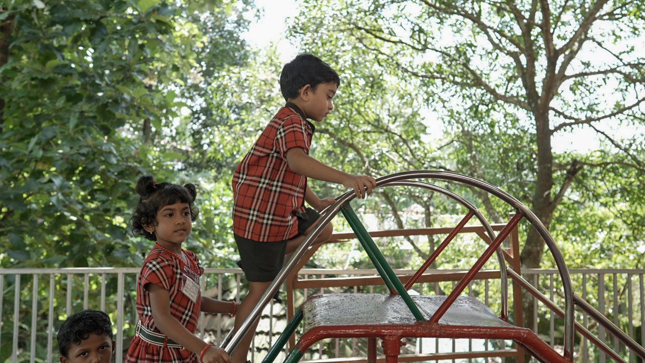 Young children in school uniform playing on a climbing slide outdoors near trees