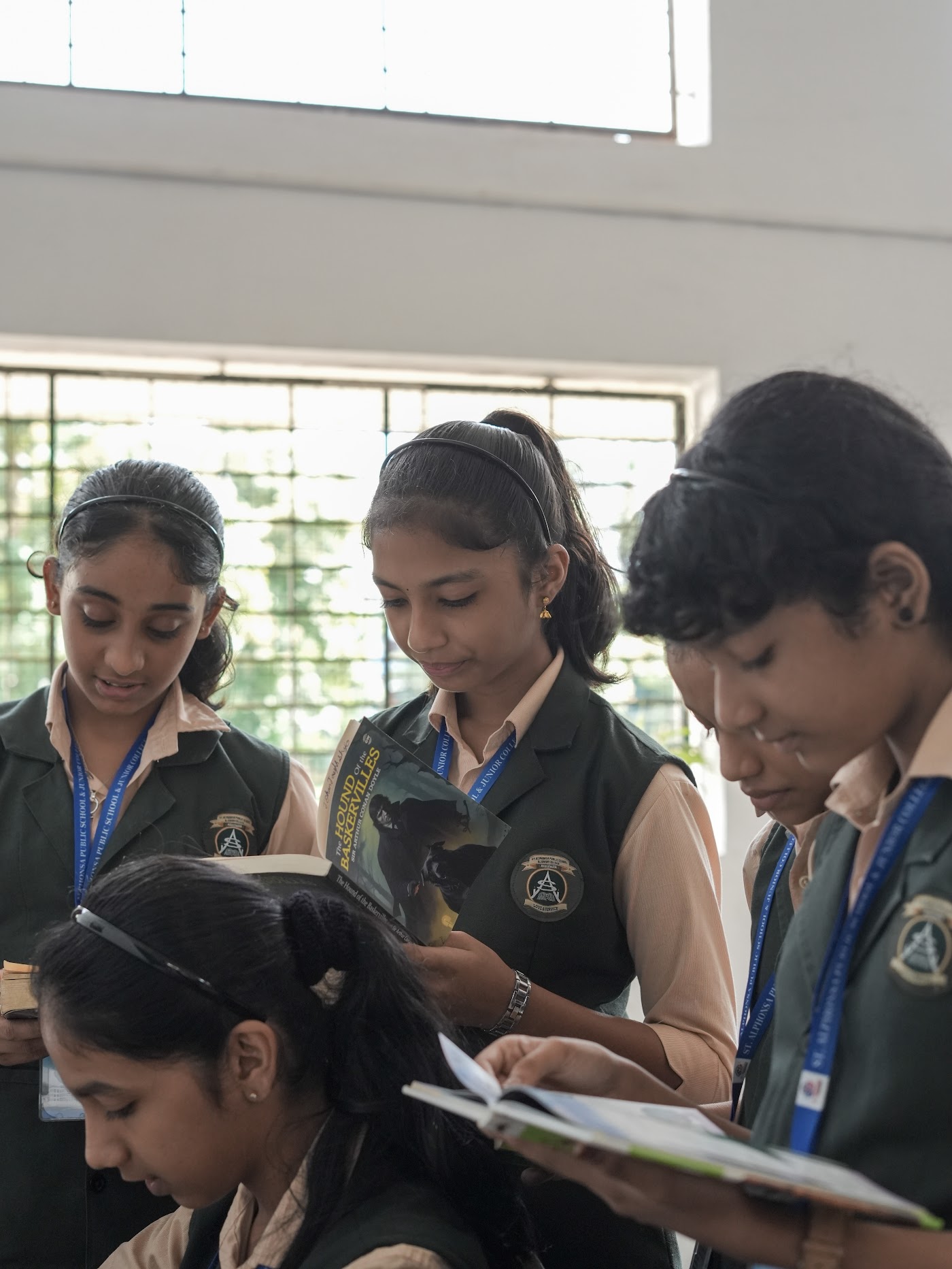 Four schoolgirls standing together and reading mystery books in the school library