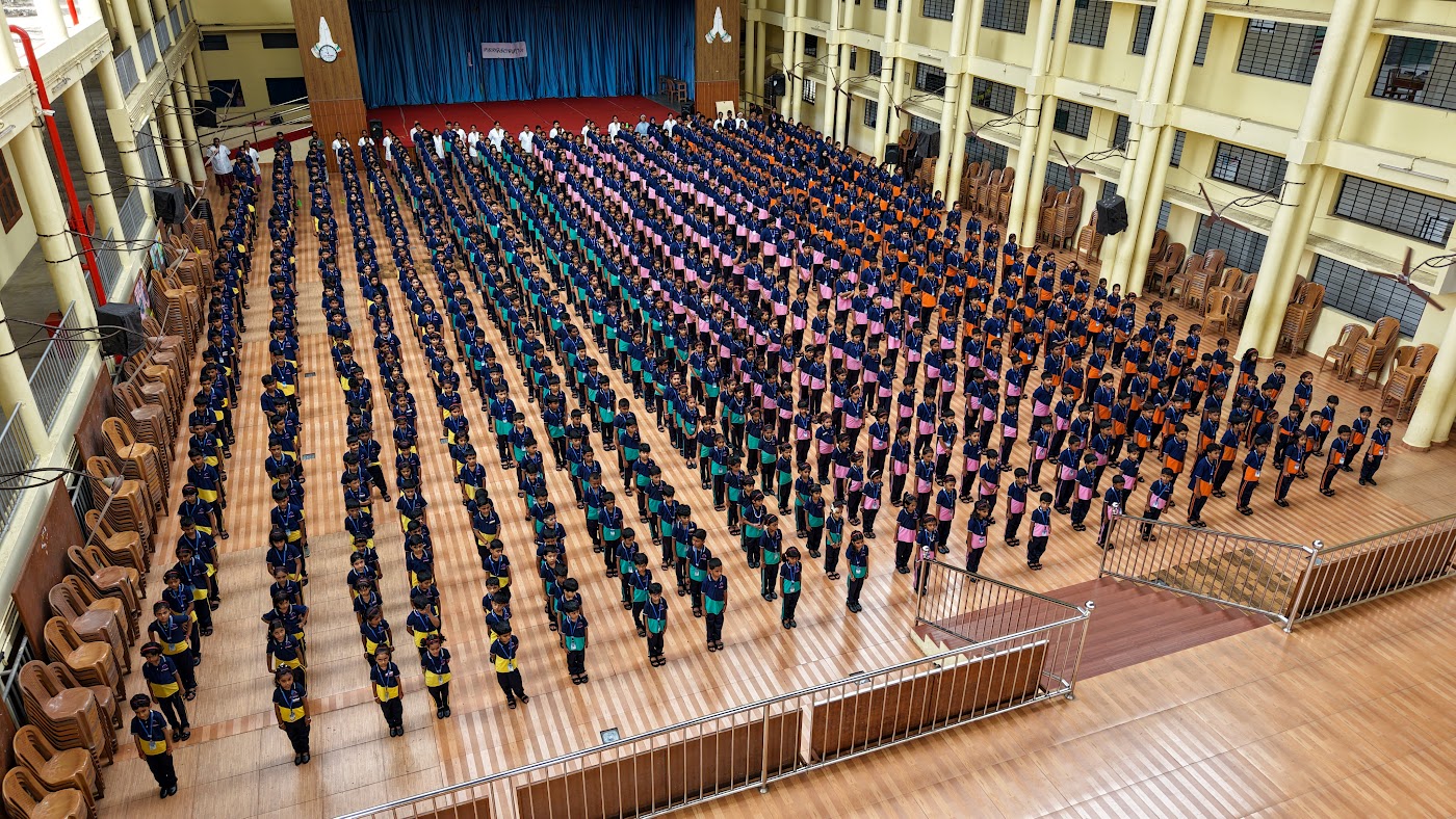 Hundreds of students standing in straight rows during morning assembly in the indoor hall