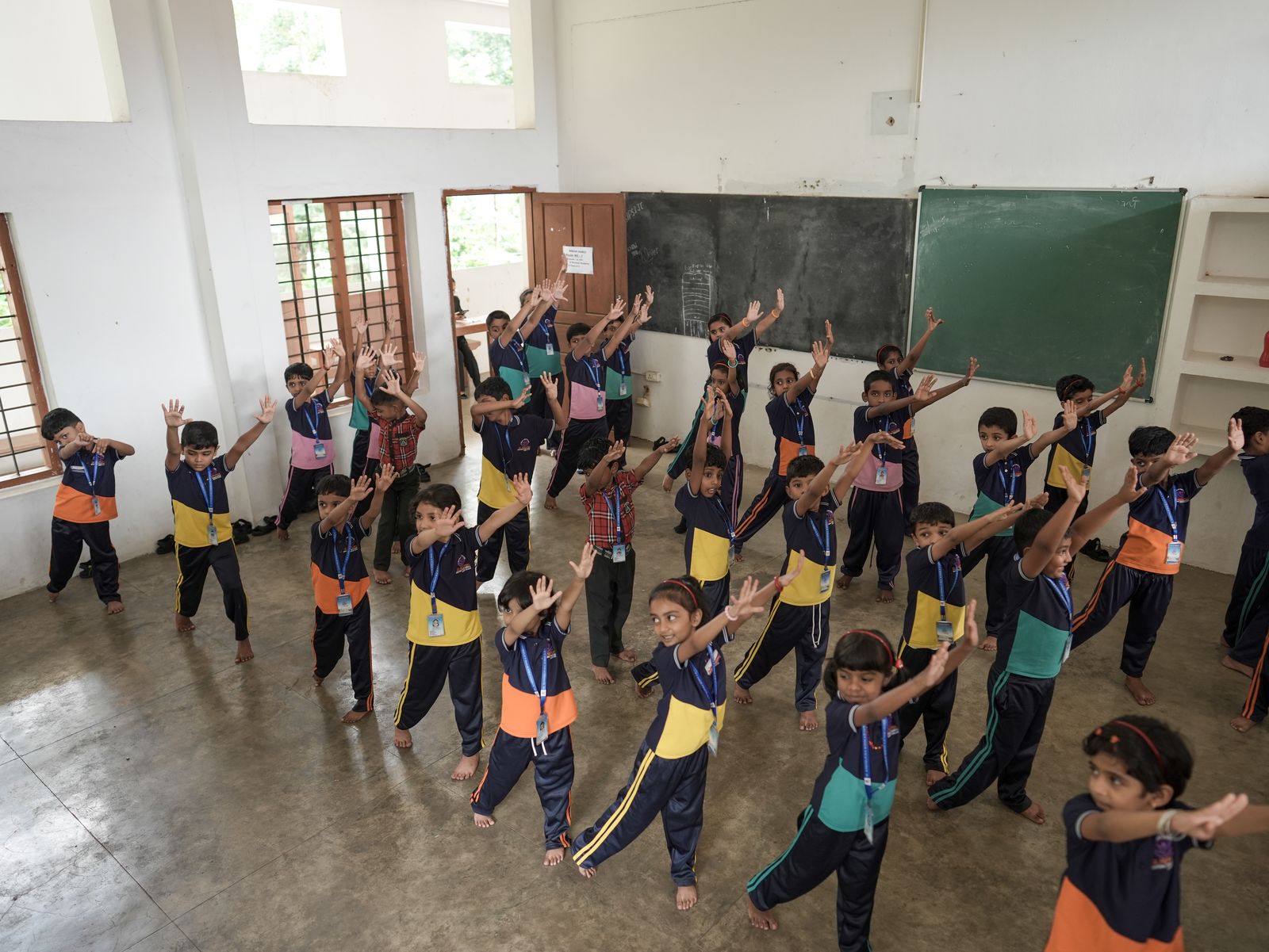 Junior school students in athletic uniforms performing stretching exercises in a hall
