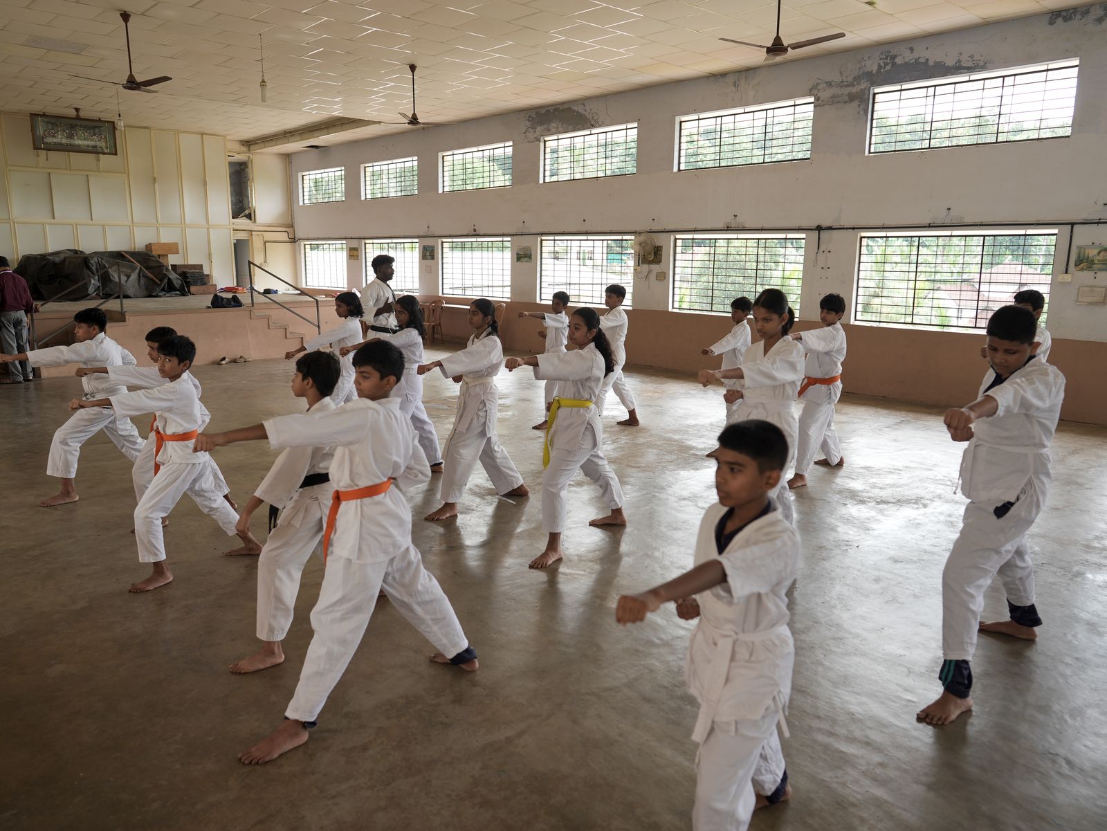 Students in white karate uniforms practicing punches in the school auditorium