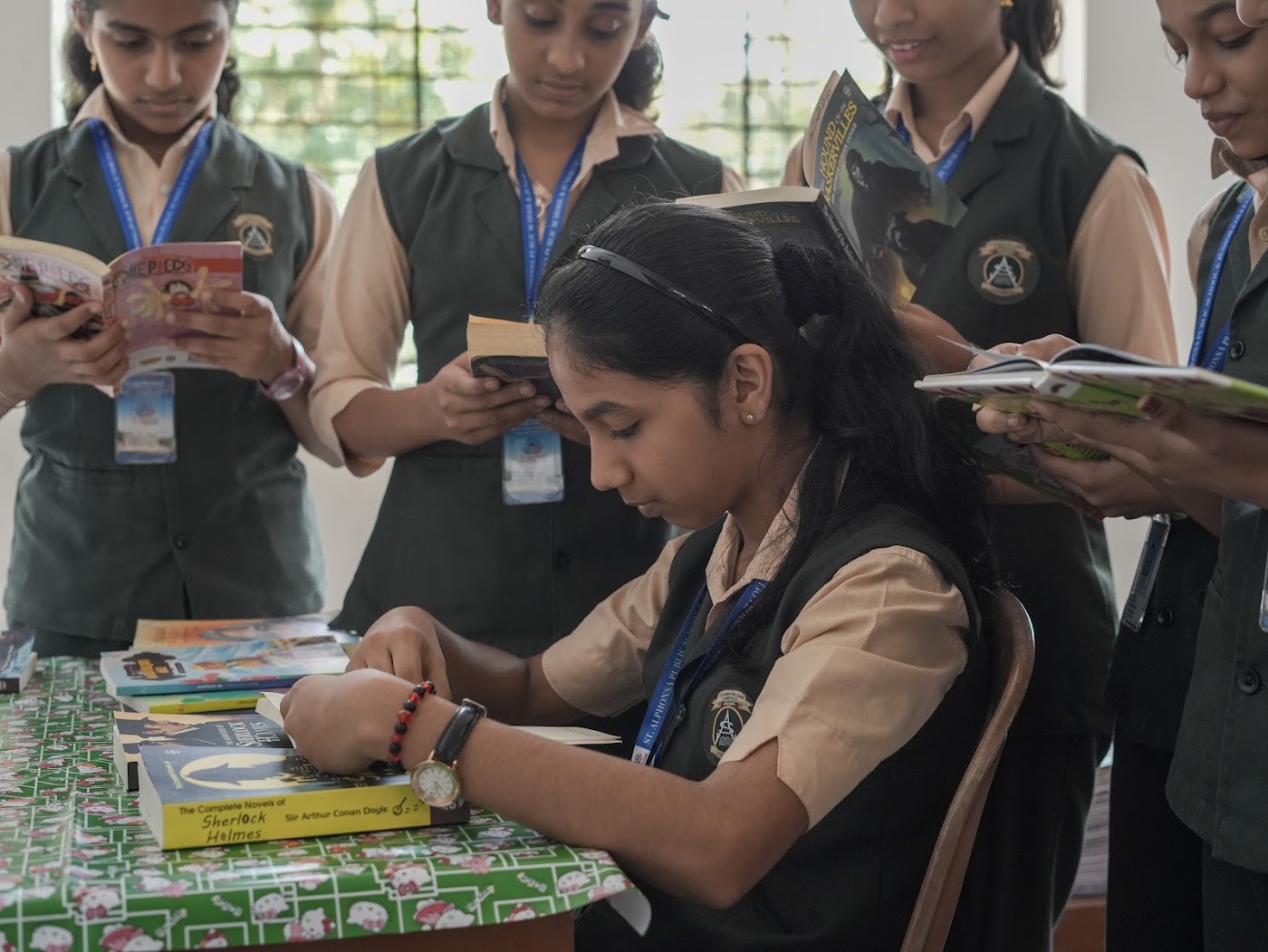 Schoolgirls reading novels together around a table in the library reading area