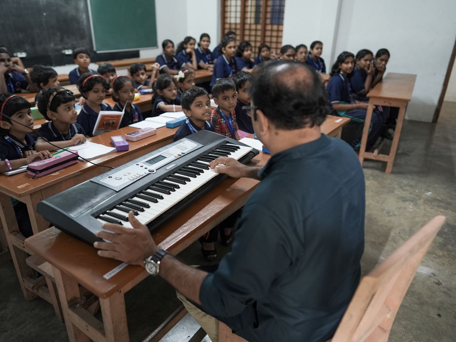 Music teacher playing an electronic keyboard for young students seated in a classroom