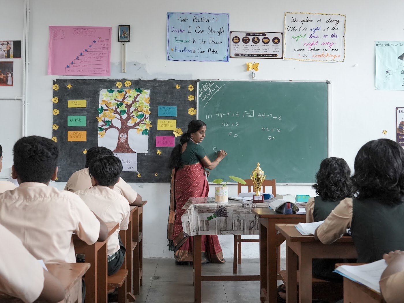 Math teacher writing arithmetic equations on a chalkboard in front of seated students