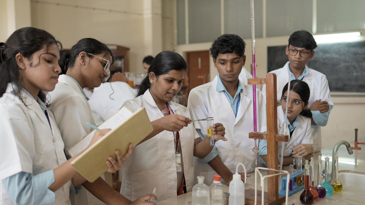 Chemistry teacher demonstrating a test tube reaction to students in white lab coats